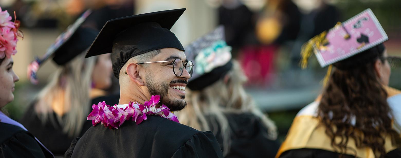 A Butte College graduate is seen wearing his cap and gown and looking towards the crows. 